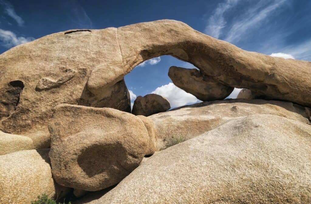 A rock that is an arch from one boulder to another with smaller boulders underneath the arch.