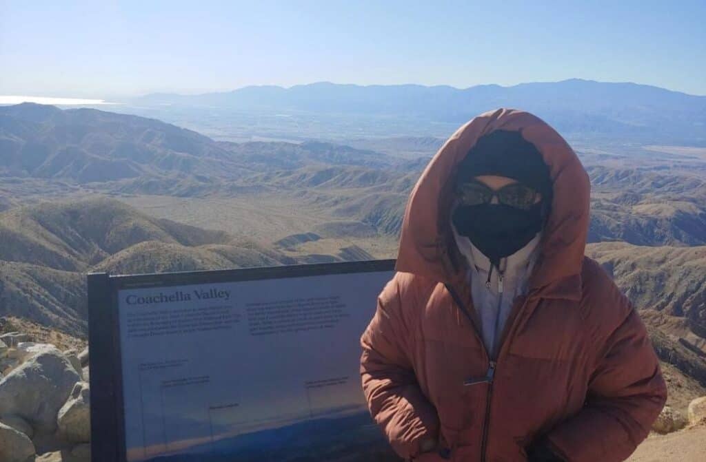 A woman bundled up in front of a sign that reads, "Coachella Valley."