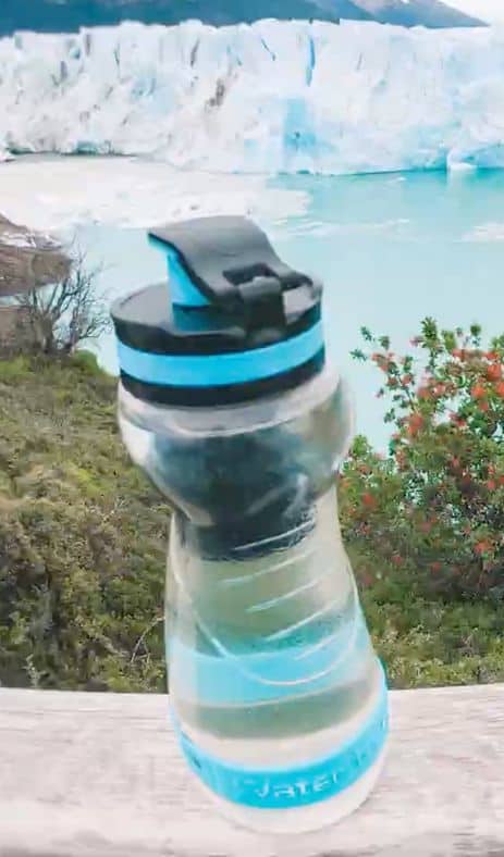 A clear water bottle sitting on a ledge with an iceberg and water in the background behind it.