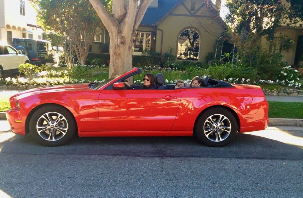 A woman in a red convertible with two kids in the back who are waving.