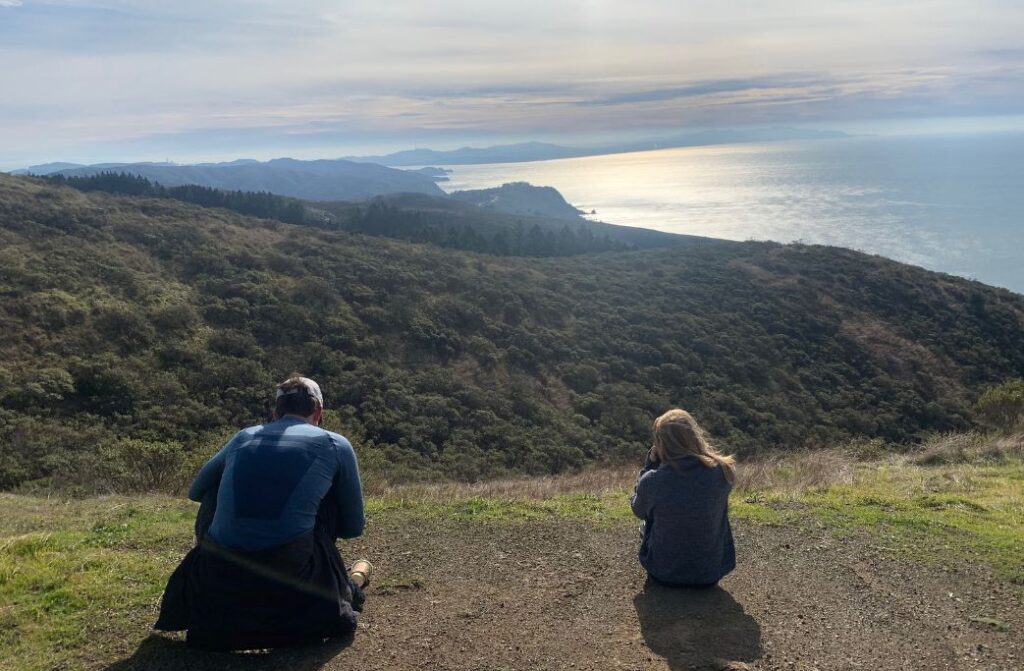 Two people sitting on the group looking at the view of the Pacific Ocean.