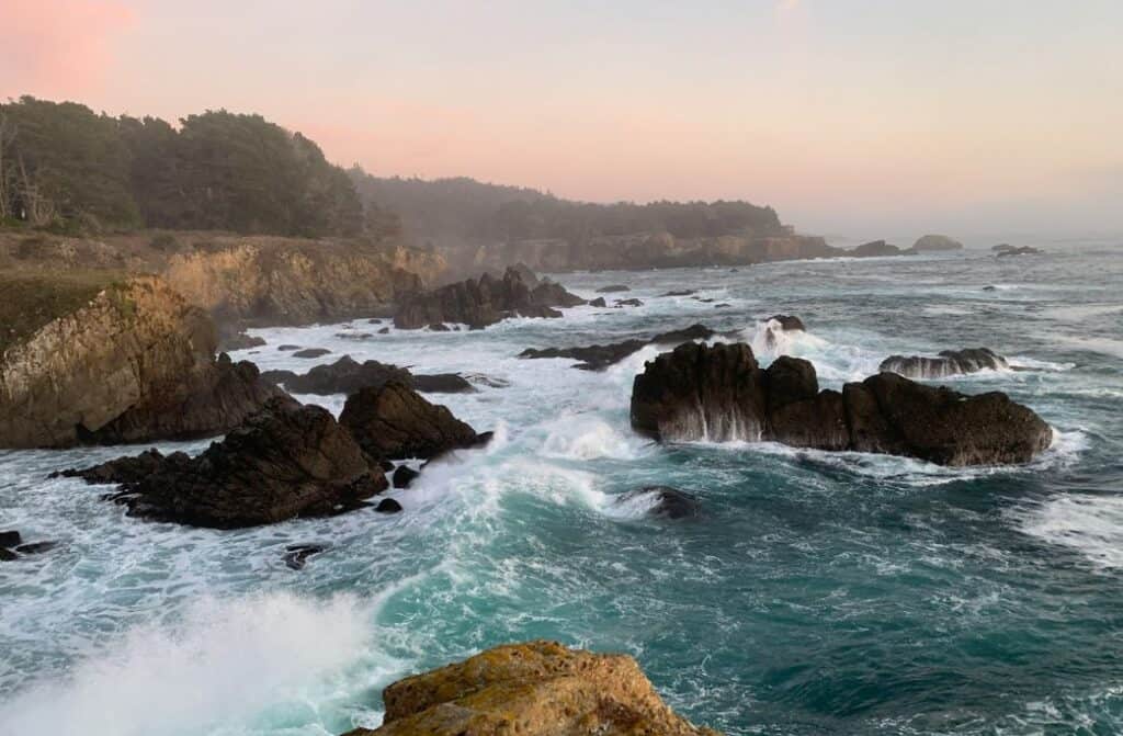 The ocean splashing against large rocks and California cliffs.