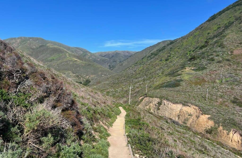 A sandy path in between green mountains.