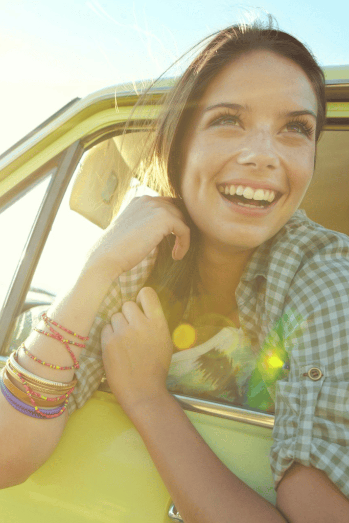 A woman leaning out the window of a yellow car, while smiling.