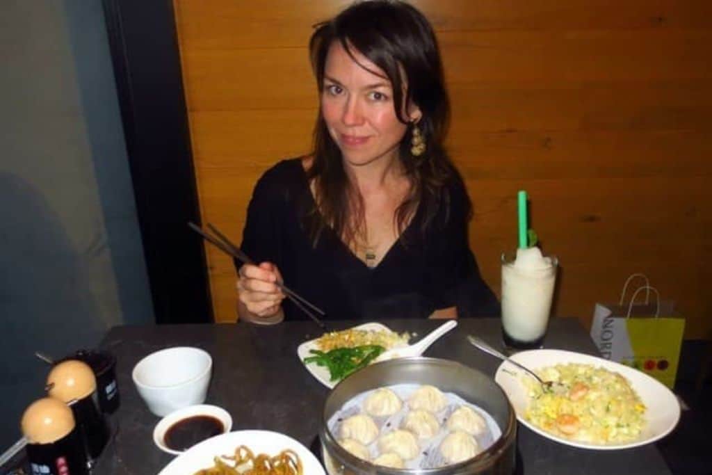 One of the pros of living in Los Angeles in all the good restaurant. A woman sits at a tale with several plates of food in front of her. She is holding chopsticks.