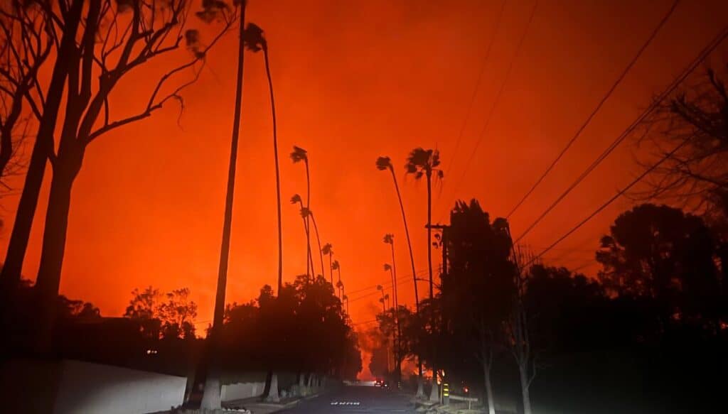 A picture of a street in pasadena with the sky a lit of flame in bright red by a raging fire