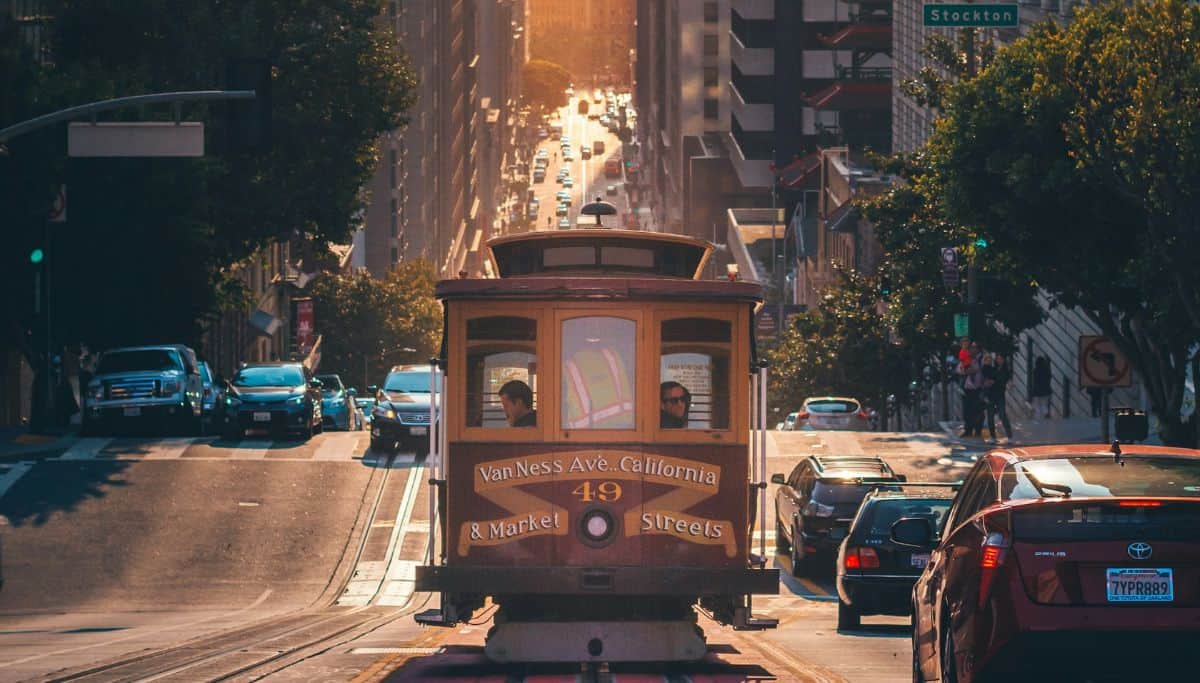 A cable car going up a hill in San Francisco as the sun sets on a busy downtown street