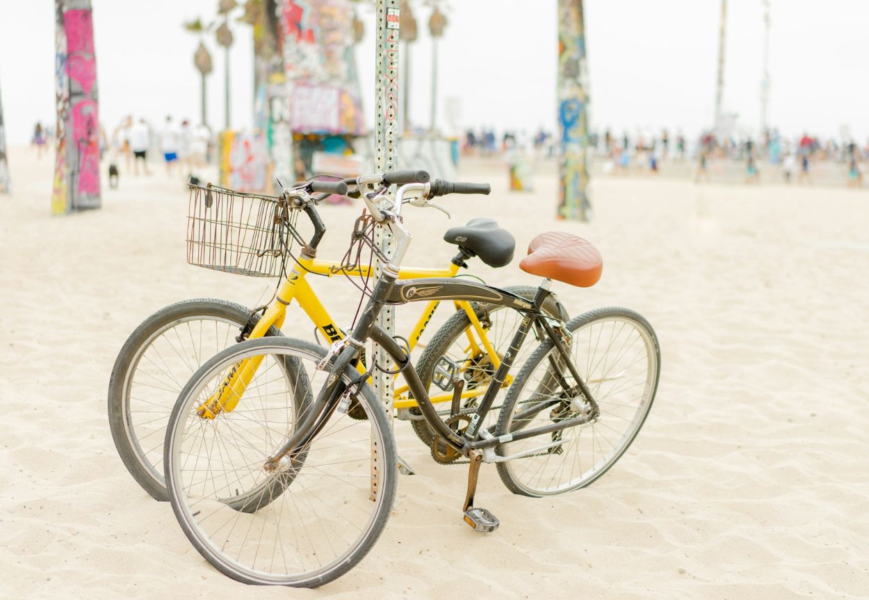 Two bikes are parked in the sand next to Venice Beach in Los Angeles.
