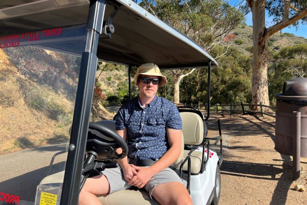 A hot man sitting in a golf cart smiling for the camera